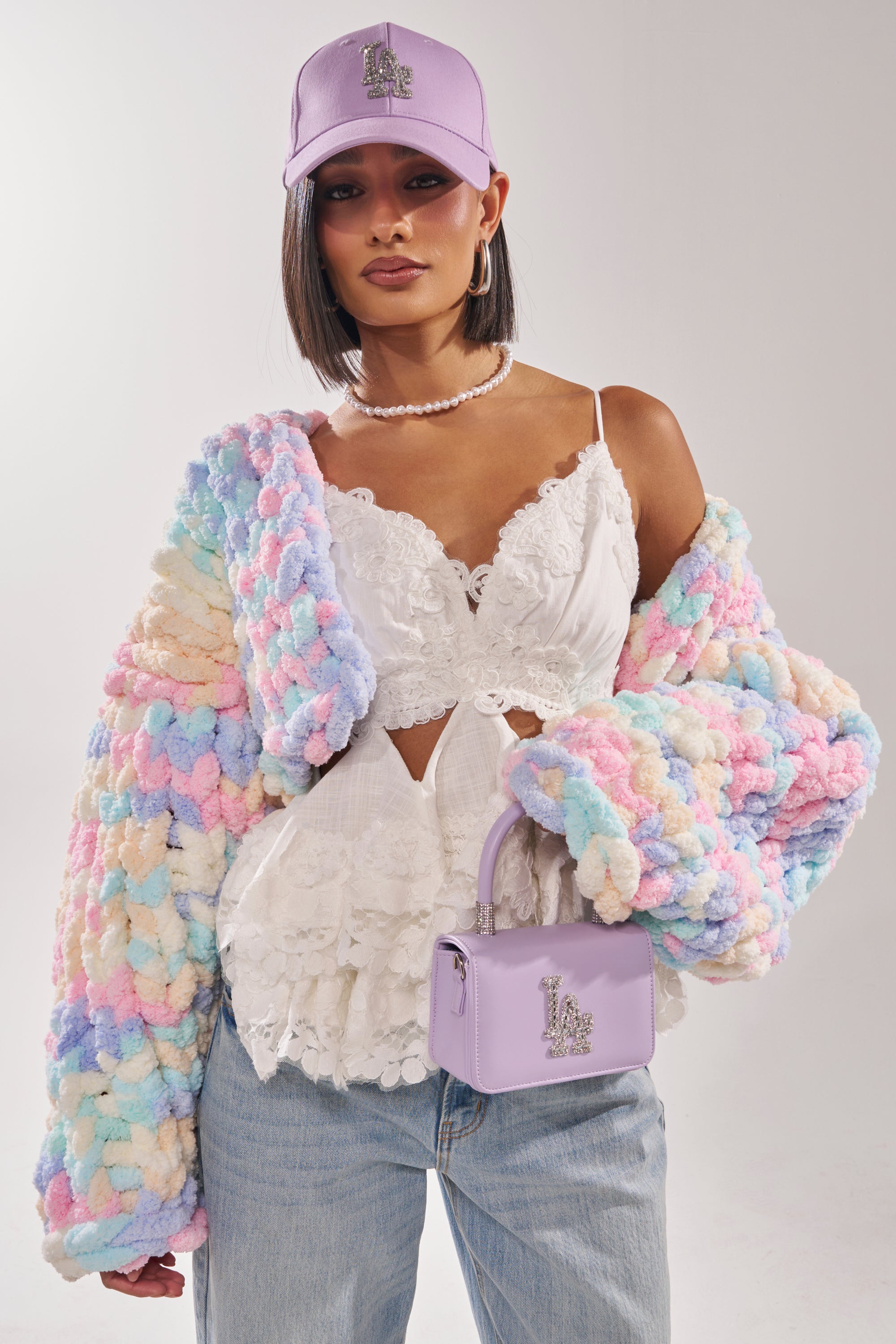 A woman wears a white top, sunglasses, and the ALIA CHUNKY CHENILLE KNIT CARDIGAN. 2