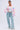 A woman stands against a plain background wearing the ALIA CHUNKY CHENILLE KNIT CARDIGAN in an oversized pastel style, paired with a white tank, light-wash wide-leg jeans with frayed seams, white sneakers, and hoop earrings.