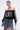 A woman styles the UNKNOWN JERSEY—a sporty-chic top with lace trim and number 83—with a layered denim mini skirt, silver jewelry, hoop earrings, and a small bag.