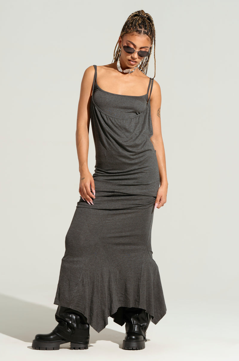 A person with braided hair stands confidently in the WYNNIE Knit Maxi Dress Set and black boots. They wear sunglasses and pose against a plain background, exuding a stylish, edgy vibe with their bodycon silhouette.