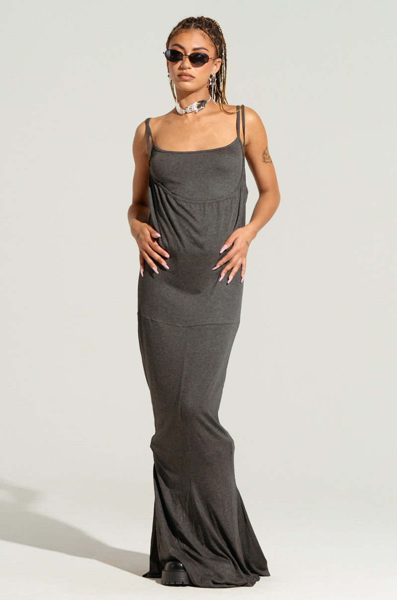 A person with sunglasses and braided hair confidently stands with hands on their midsection while wearing the WYNNIE KNIT MAXI DRESS SET, a long, dark grey bodycon maxi dress crafted from super stretchy fabric. They complete the look with a choker necklace and black shoes.