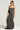 A person wearing sunglasses and the WYNNIE KNIT MAXI DRESS SET in dark gray stands against a neutral background. With braided hair, a necklace adds to their look, while a tattoo on their upper arm accentuates the sleek bodycon silhouette of the dress.