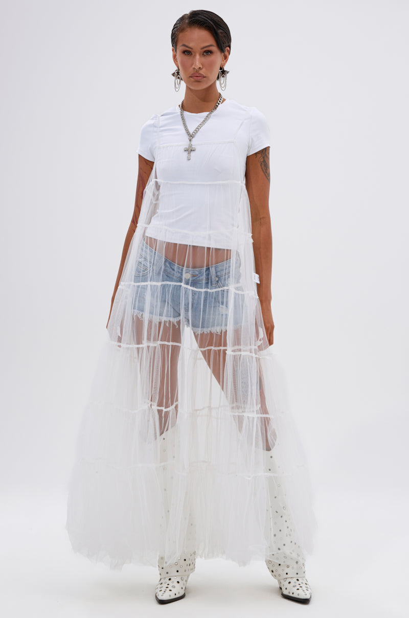 A person stands against a white background wearing the PERFECT FOR LAYERING TULLE MAXI DRESS IN WHITE over a white t-shirt and denim shorts, paired with white patterned boots and layered necklaces, including a cross pendant. 2