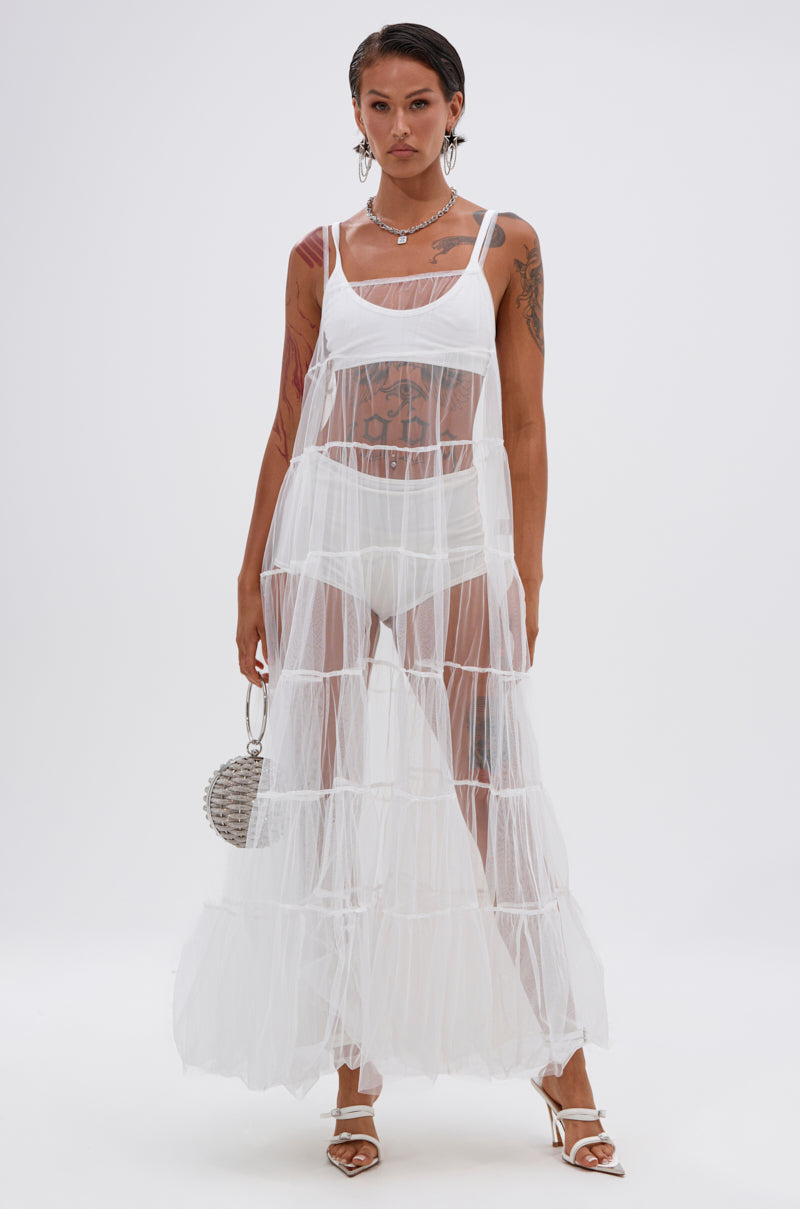 A person stands against a white background wearing the PERFECT FOR LAYERING TULLE MAXI DRESS IN WHITE over white undergarments, styled with silver jewelry, a small round bag, and heeled sandals. 3