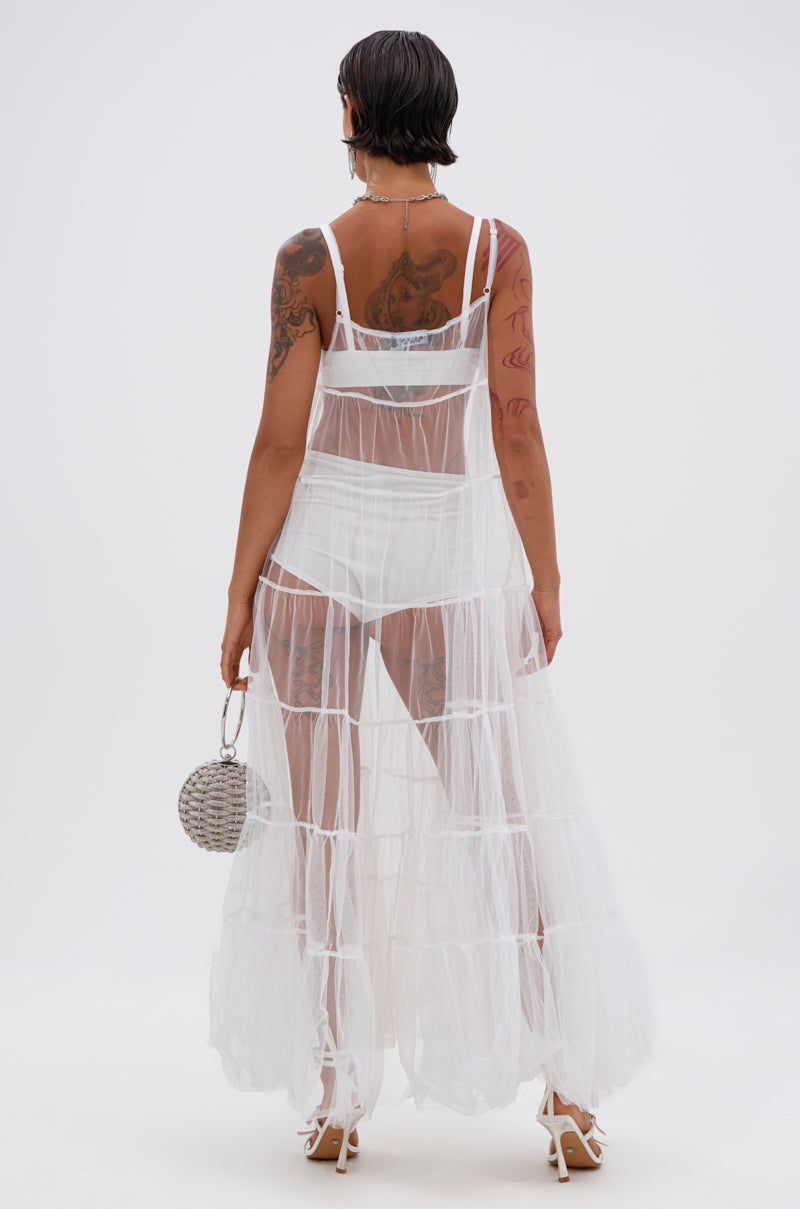 A person with short dark hair and tattoos wears the PERFECT FOR LAYERING TULLE MAXI DRESS IN WHITE over white underwear, with a silver handbag and high heels, standing against a plain background facing away. 5