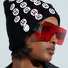 Wearing oversized red sunglasses and a black I REALLY DO BEANIE adorned with "I ❤️ ME" badges, a person completes their look with a black and white striped jacket. The side profile image showcases the beanie's stretchy knit, adding coziness to this statement ensemble.