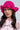 A woman with long dark hair wears the CROCHET NIGHTS HAT, featuring a bright pink hue and ruffled brim, paired with a light pink 