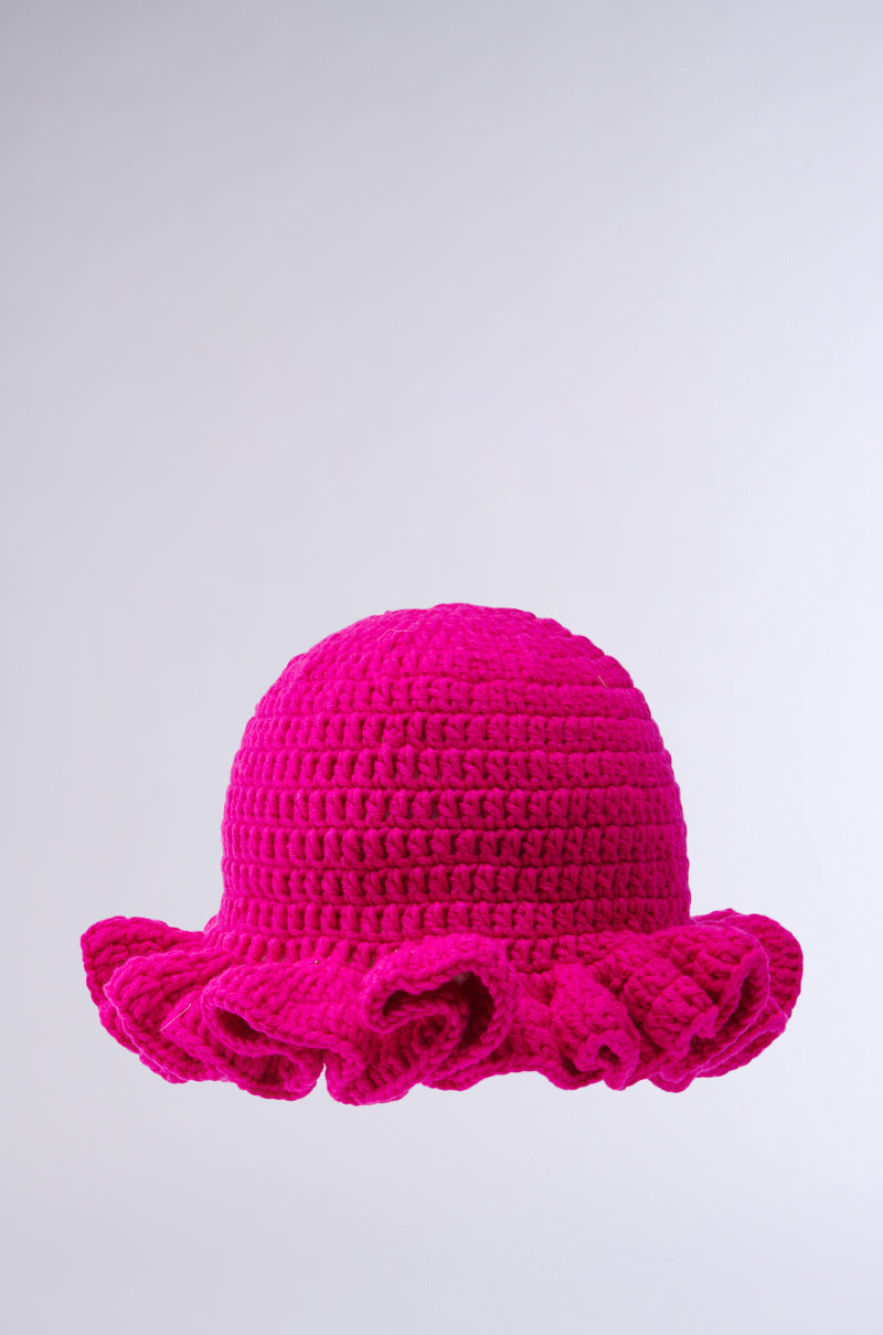 The CROCHET NIGHTS HAT, in bright pink with a round crown and wide ruffled brim, is beautifully crochet knit and displayed against a plain light gray background.
