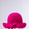 The CROCHET NIGHTS HAT, in bright pink with a round crown and wide ruffled brim, is beautifully crochet knit and displayed against a plain light gray background.