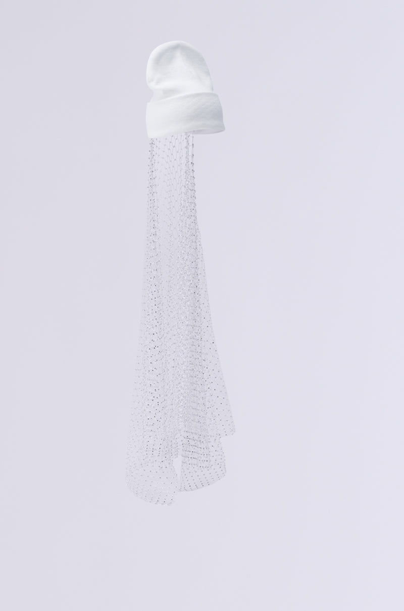 The TRAIL OF RHINESTONES BEANIE, characterized by its white rhinestones and complemented by a long, transparent veil, displays a delicate netted pattern with subtle rhinestone accents. This sophisticated accessory stands out against a light gray background, offering a striking contrast to the solid texture of the knit beanie. 6