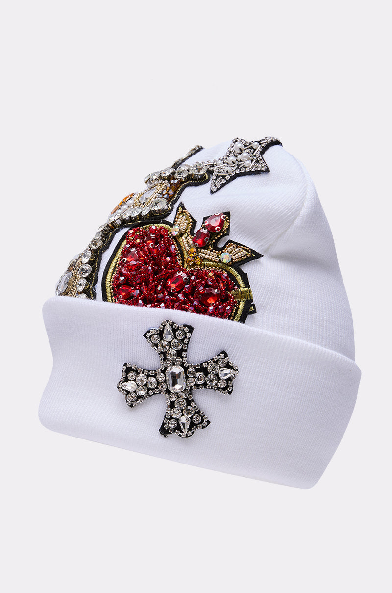 The NO ONE ELSE LIKE ME BEANIE is a white knit beanie decorated with rhinestones, beads, a bold red heart, gold and silver accents, and jeweled silver crosses on both the front and folded brim. 4