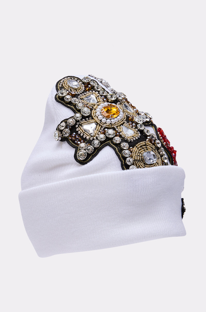 The NO ONE ELSE LIKE ME BEANIE is a white knit beanie embellished with gold, silver, and clear rhinestones and ornate embroidery in a decorative pattern. 5