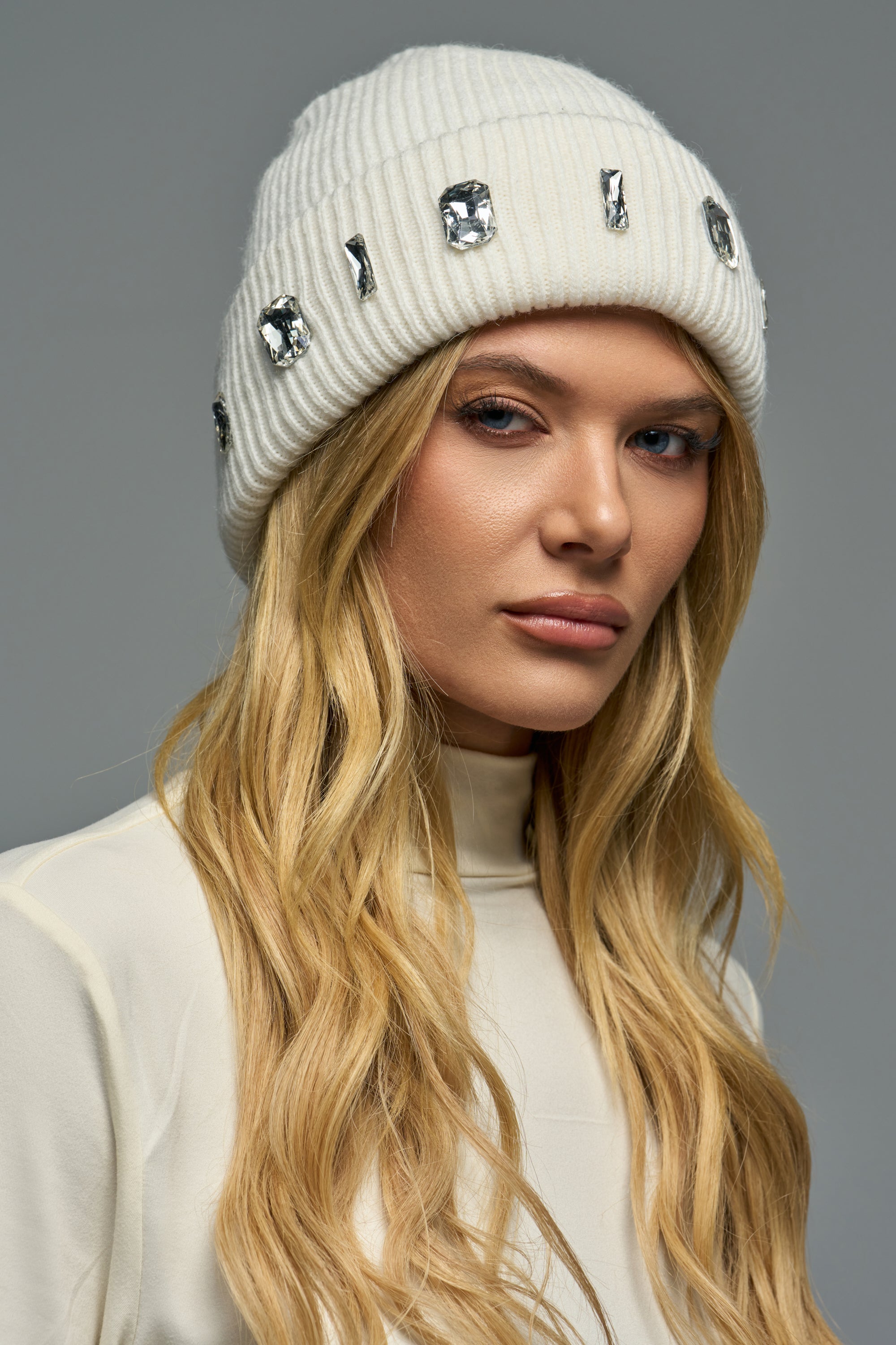 Woman wearing an AVERY EMBELLISHED HAT, a cream-colored knit beanie embellished with scattered clear crystals.