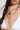 Wearing the DOG TAG BUT MAKE IT CUTE NECKLACE, a person elegantly showcases the three-layer design featuring uniquely styled silver dog tags. The necklaces, embellished with sparkling rhinestones, drape gracefully over a white bikini top, while their hair falls gently over one shoulder, perfectly highlighting both the dazzling accessories and chic attire.