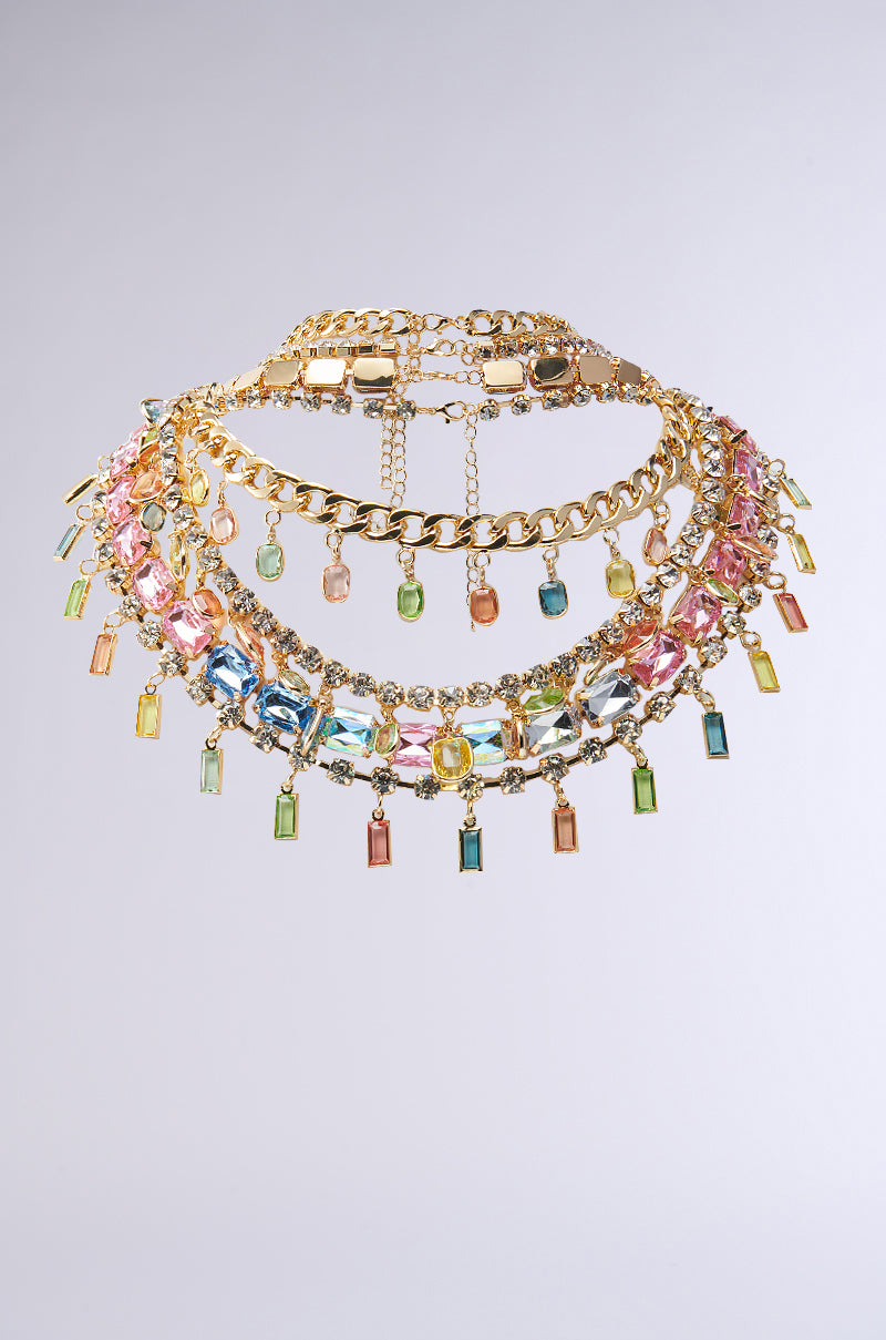 The FEEL MY COLORS NECKLACE SET features a gold chain with vibrant jewels in pink, blue, green, and yellow hues. Its layered design adds an intricate elegance to any plain outfit.