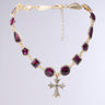 The INSPIRE ME CROSS NECKLACE by AKIRA Label features a silver cross pendant adorned with small diamonds and a rhinestone trim, showcasing an intricate design of variously shaped purple gemstones linked ornately. It has an adjustable chain clasp and is set against a soft gradient background.