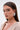 A woman with straight brown hair models the ALL MY HEART EARRING IN SILVER—large, heart-shaped earrings adorned with crystals—wearing neutral makeup and a shimmery light beige top, looking over her shoulder against a plain background.