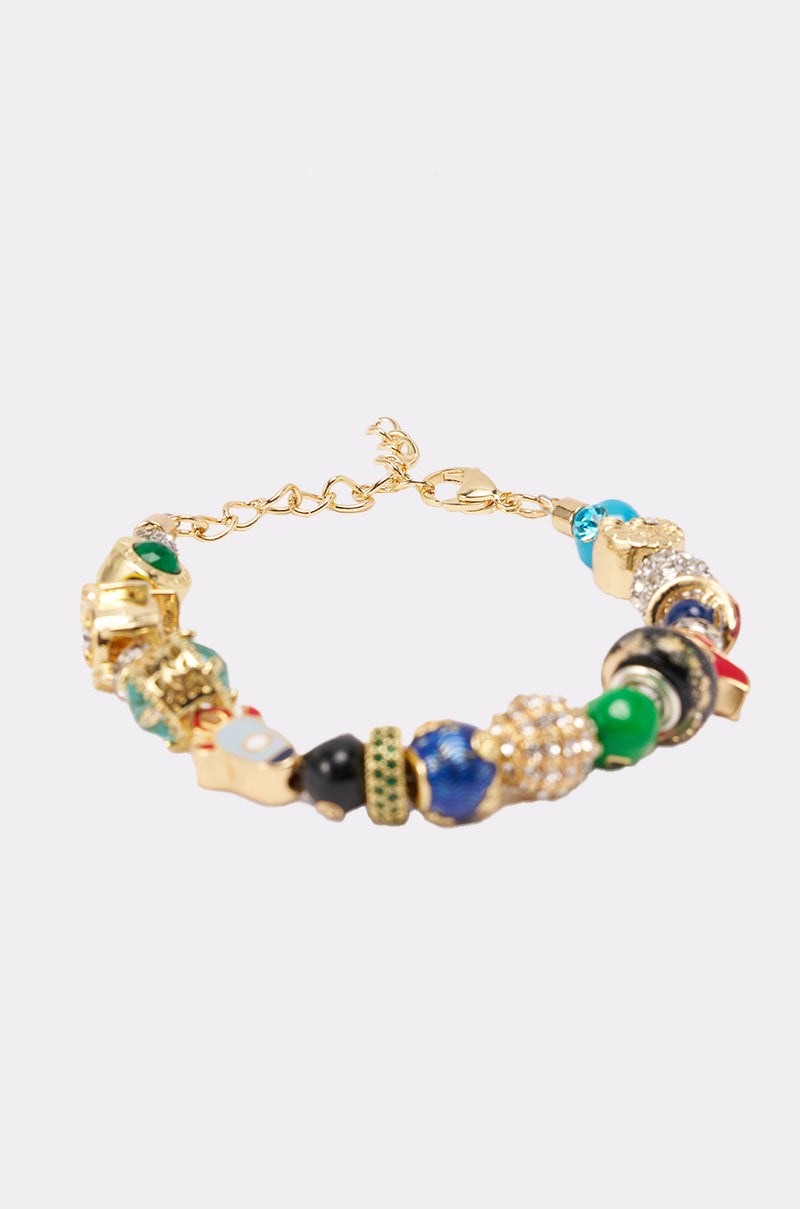 The SPACED OUT CHARM BRACELET features a gold-tone chain with blue, green, black, and gold charms and beads, shown against a simple light background. 2