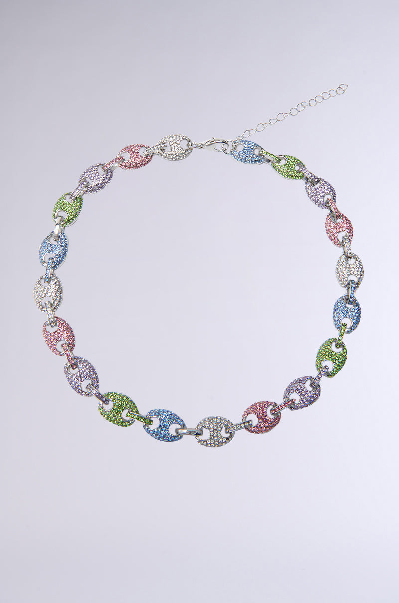 The HE LOVES ME NECKLACE features linked oval segments with sparkling rhinestones in white, pink, green, blue, and lavender. Two interlocking loops form a stunning circular chain, secured with an adjustable lobster clasp.