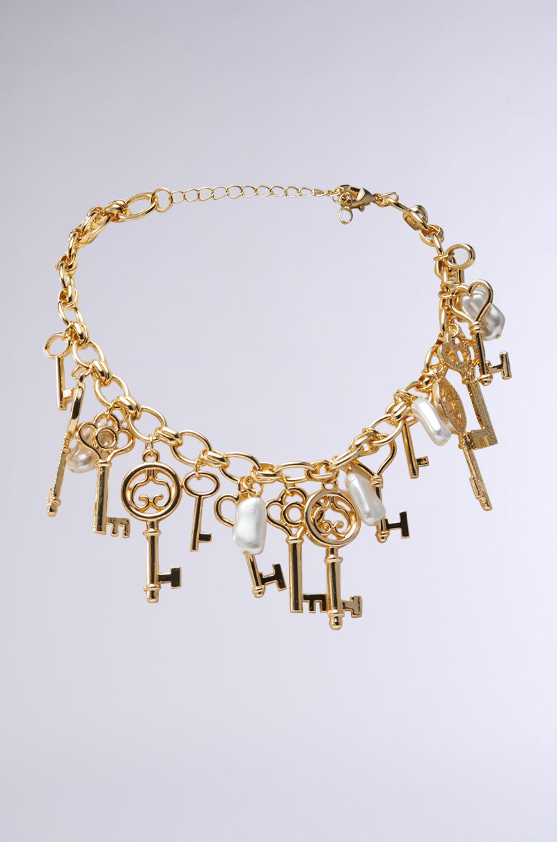 The YOU HAVE THE KEY CHARM NECKLACE features a gold metallic chain embellished with ornate keys of various sizes and designs, accented by pearls, all connected in a stylish arrangement against a plain backdrop.