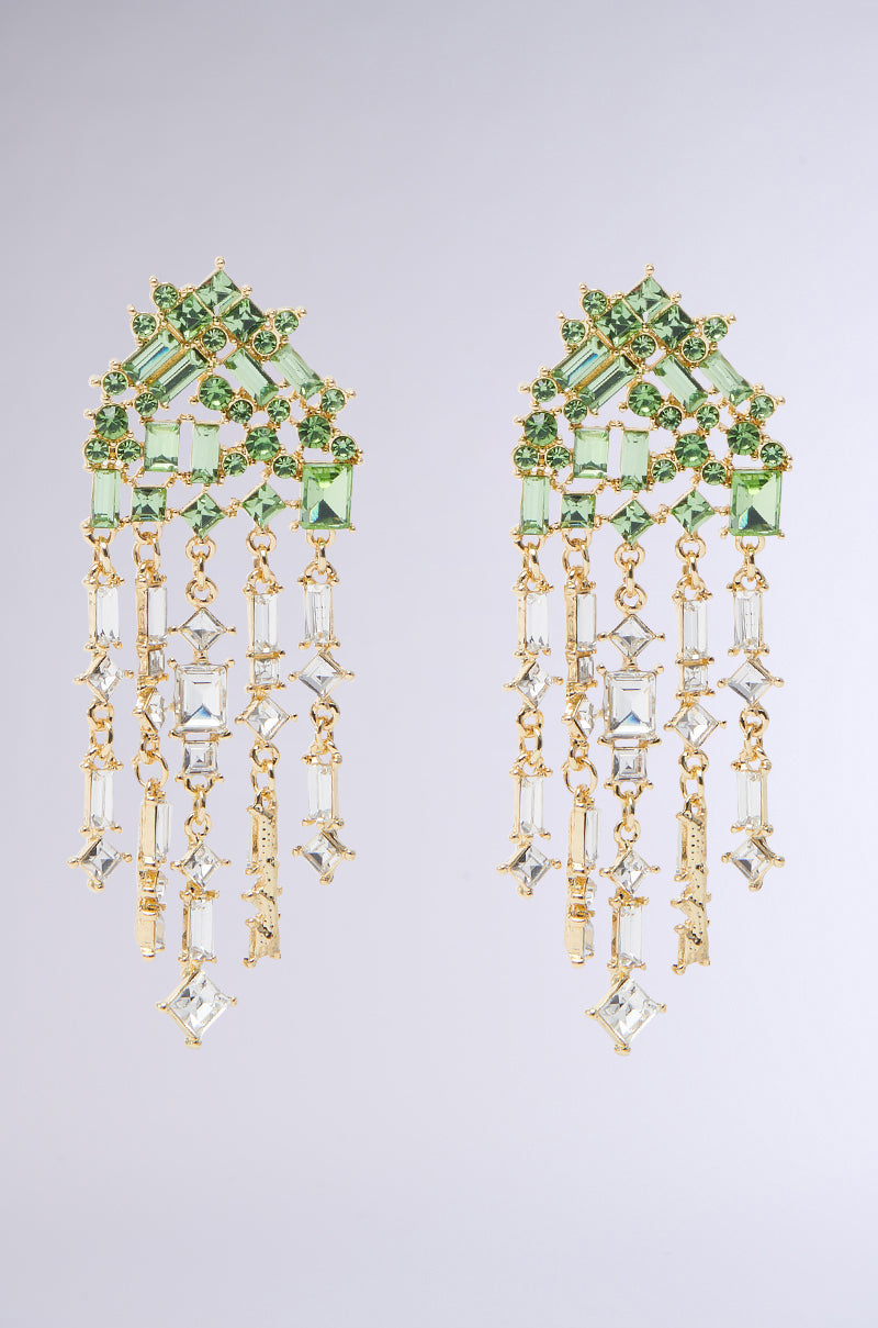 The BLING ME HOME EARRING features ornate chandelier style with emerald green gemstones in gold, geometric patterns at the top, and a cascading dangle of clear rectangular crystals. 0