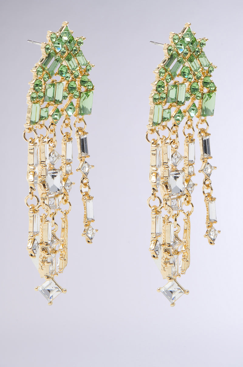 The BLING ME HOME EARRING showcases a cascading dangle silhouette with emerald green gemstones at the top and clear rectangular and square gems beneath, set on a light gray background. 3