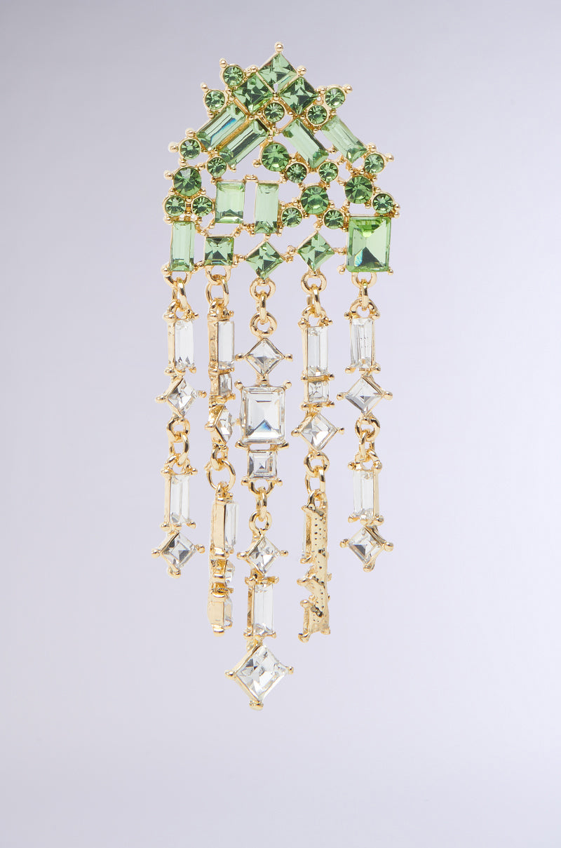 The BLING ME HOME EARRING showcases emerald green gemstones in a geometric top, finished with cascading gold chains and clear rectangular and square crystals against a plain light gray background. 4