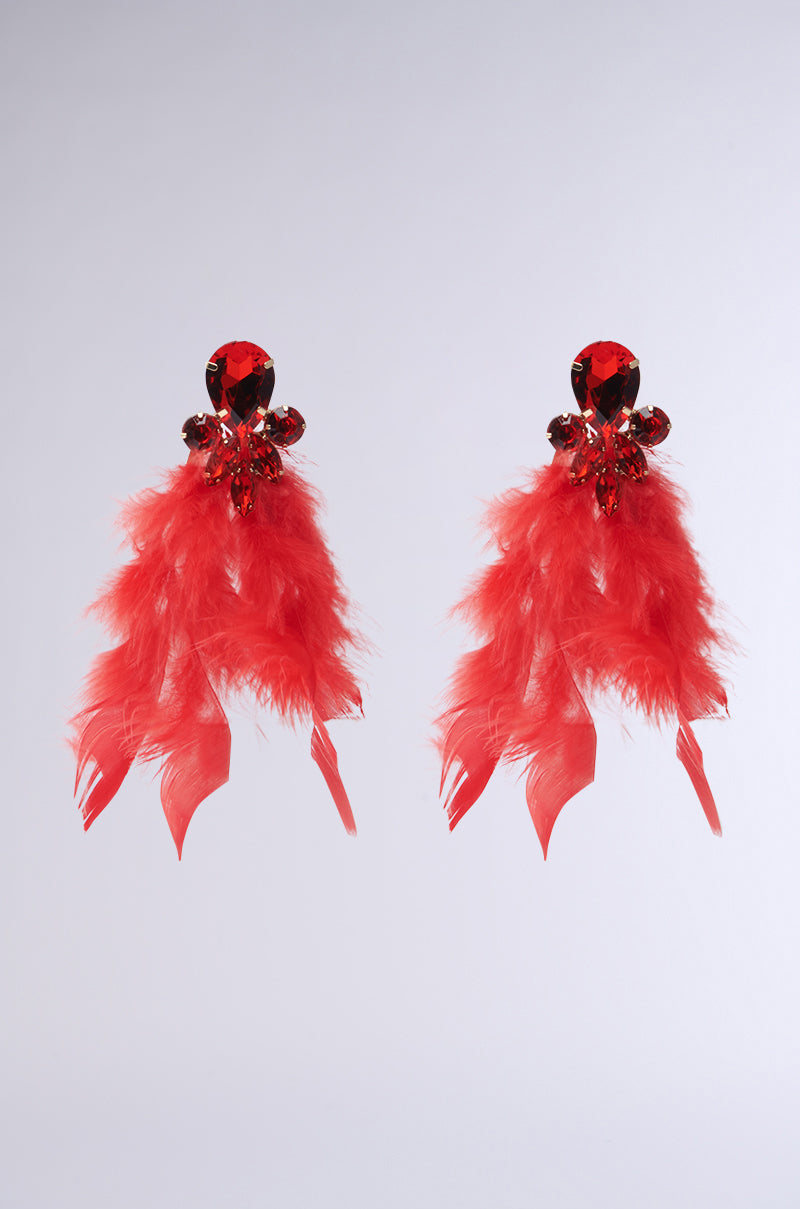 The SEE RED FEATHER EARRING by AKIRA Label features vivid red cascading feathers with ornate crystal tops on a plain white background, offering a dramatic and luxurious ruby-inspired teardrop design.