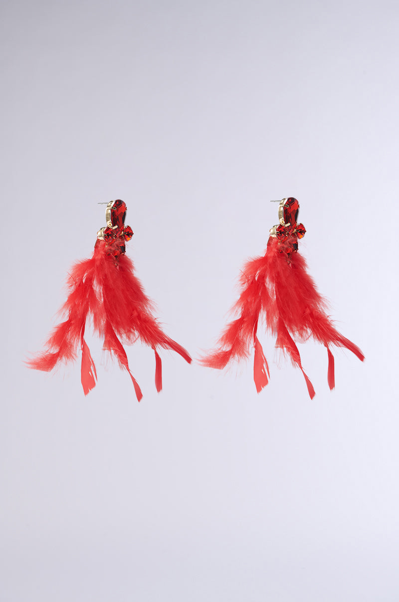 The SEE RED FEATHER EARRING by AKIRA Label showcases vibrant feathers attached to a gold-tone base, accented with ruby-inspired teardrop gemstones. The feathers fan out elegantly for a bold and striking look against any background.