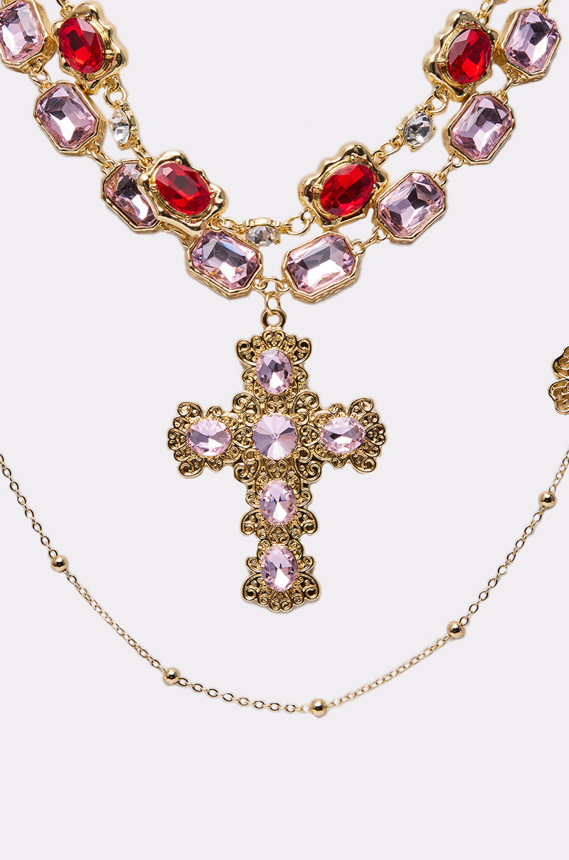 The LAYERED UP NECKLACE features a faux gold design with large red and pink gemstones, a decorative cross pendant with pink stones, and a delicate beaded gold chain for a chic layered look. 3