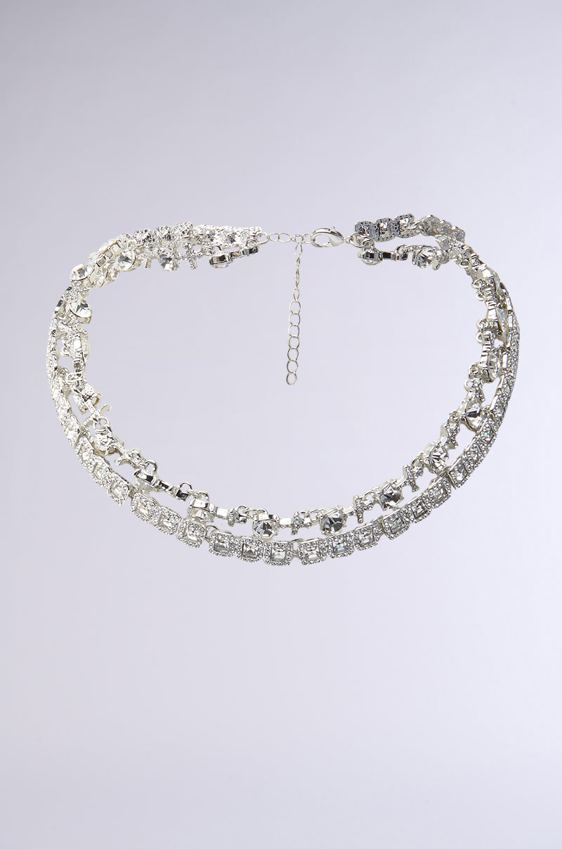 The BLING RING NECKLACE IN SILVER features two rows of square and round clear rhinestones, creating a sparkling faux silver bling look, displayed on a plain light gray background. 1