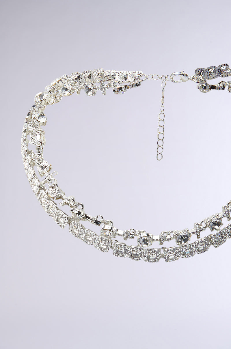A close-up of the BLING RING NECKLACE IN SILVER, a double-layered faux silver necklace featuring sparkling round-cut rhinestones, displayed against a light gray background. 5