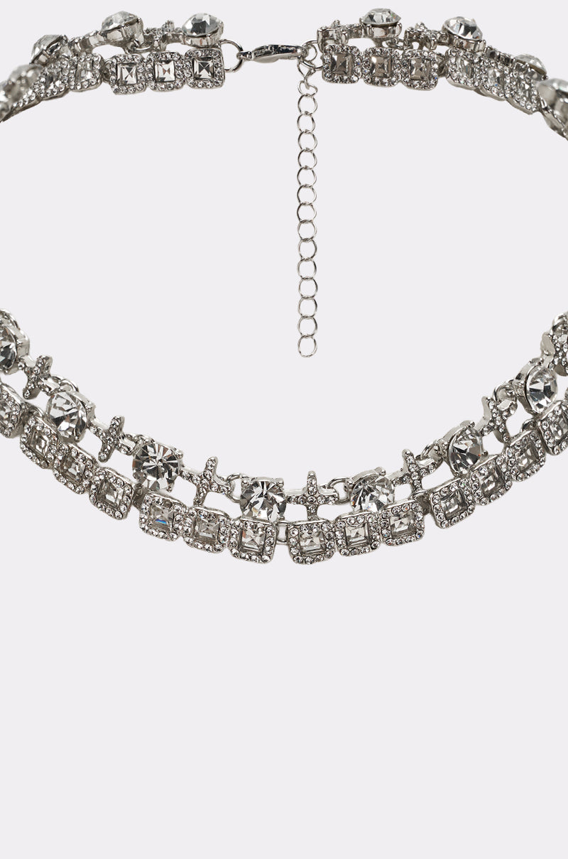 A close-up of the BLING RING NECKLACE IN SILVER, showcasing sparkling large and small clear rhinestones with an adjustable chain clasp, set against a plain light background. 3