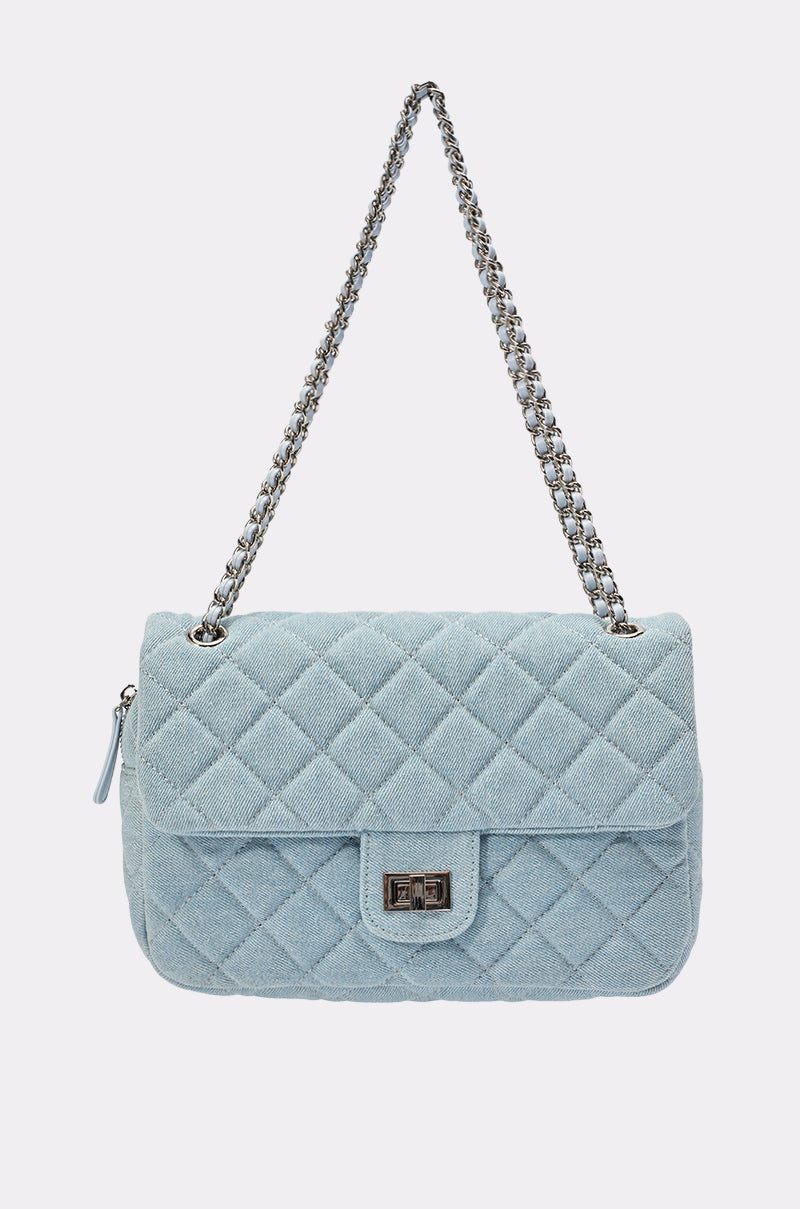 The BLUE JEAN BABY DENIM QUILTED PURSE is a light blue quilted denim shoulder bag with a silver chain strap and rectangular twist-lock closure, shown on a plain white background. 0
