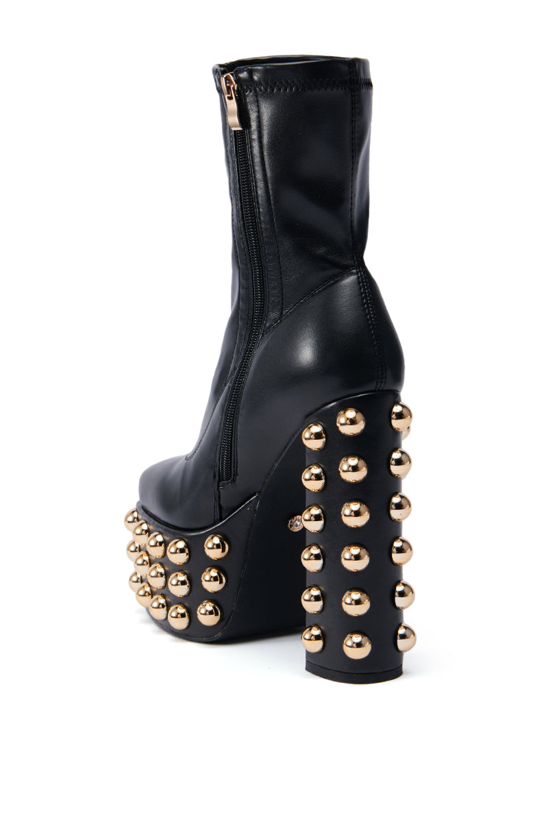 The AZALEA WANG AKITO CHUNKY BOOTIE is a black high-heeled faux leather boot with a side zipper, adorned with chunky gold studs on the platform and heel.