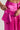 A person is revealing a hidden pocket inside the vibrant pink satin A MOMENT APART WIDE LEG TROUSER WITH POCKETS IN PINK from the AKIRA Label. The pocket features a flap with a snap button and an additional strap. The close-up image highlights the texture and sheen of the utility pant fabric.