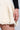 A person wearing the QUINN PLEATED TWEED MINI SKIRT, featuring a textured cream high-rise design with a frayed edge, paired with a black long-sleeve top. The image focuses on the lower part of the skirt, capturing the details of the fabric and hemline.