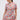 A woman in the PRETTY IN PINK BROCADE BEADED MINI DRESS with short sleeves and pastel floral brocade looks down to her left. Her long hair is in a ponytail, and she finishes the look with statement earrings.
