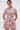 A woman showcases the PRETTY IN PINK BROCADE BEADED MINI DRESS, featuring short sleeves and a bold floral pattern. Her slicked-back hair, gold earrings, and striking makeup pop against a plain white background.
