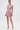 A woman poses against a white backdrop in the PRETTY IN PINK BROCADE BEADED MINI DRESS, her hair slicked back and styled with gold heels and drop earrings for an elegant finish.