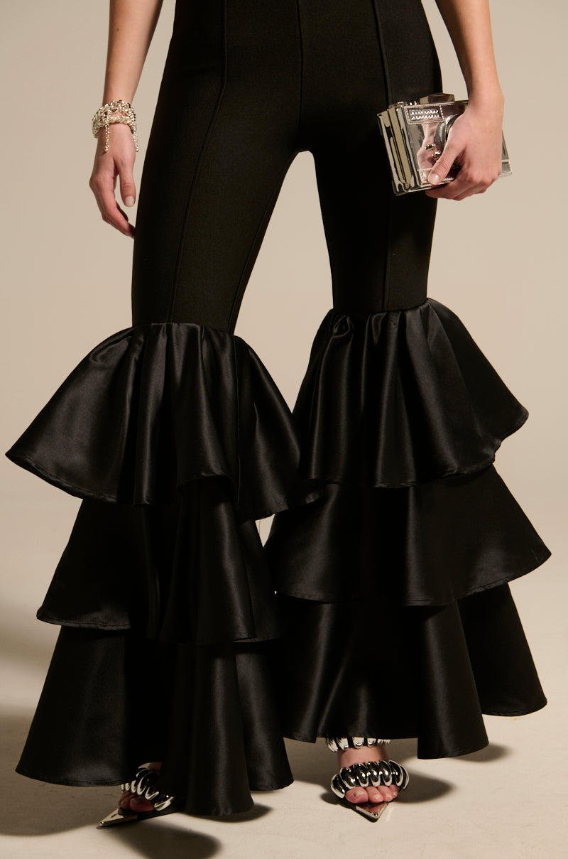 Rocking the "I JUST WANNA DANCE FLARE LEG JUMPSUIT," the person complements their look with a metallic clutch, silver bracelets, and stylish black open-toe heels adorned with unique embellishments.