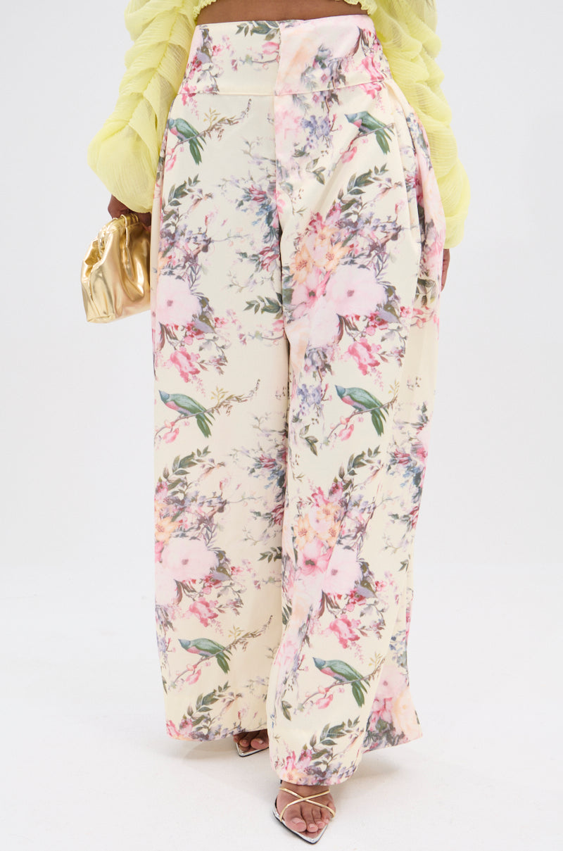 Wearing SABRINA FLORAL WIDE LEG PANT with a vintage pink, green, and purple design, the person pairs them with a gold handbag and a pale yellow top on a plain white backdrop. 2