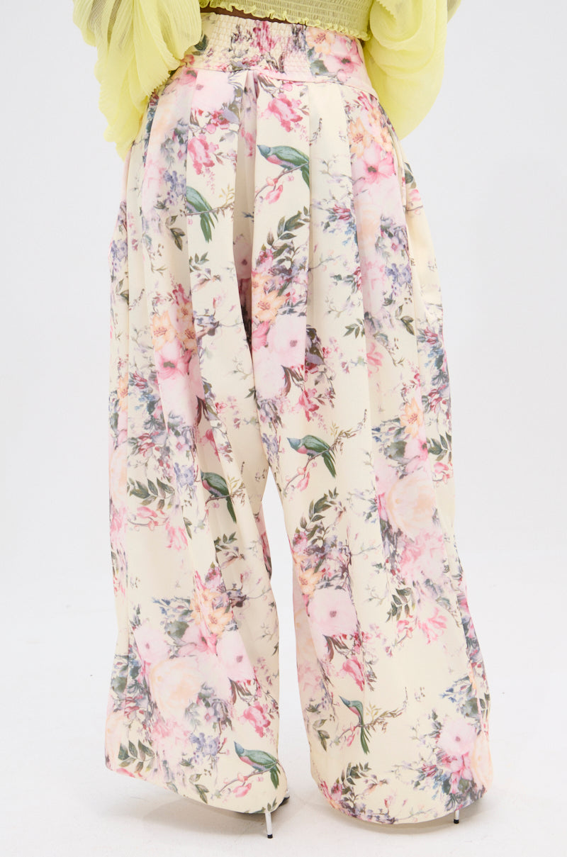 The SABRINA FLORAL WIDE LEG PANT in pinks, greens, and whites is paired with a sheer pale yellow top, beautifully complementing its high-rise waist against a plain white background. 4