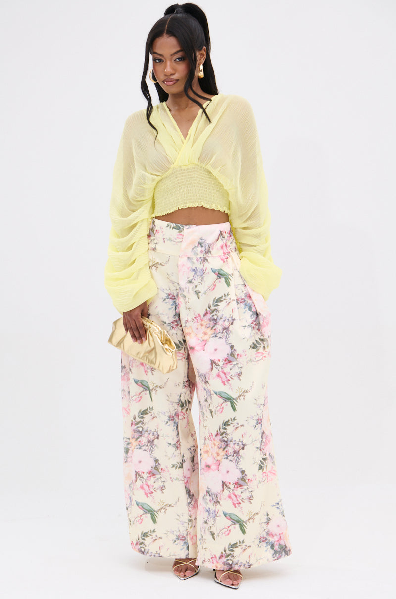 Against a plain background, a person confidently wears sheer yellow sleeves with SABRINA FLORAL WIDE LEG PANTS, clutching a shiny gold purse. Strappy heels and sleek long hair accentuate the high-rise waist of this vintage-inspired outfit. 5