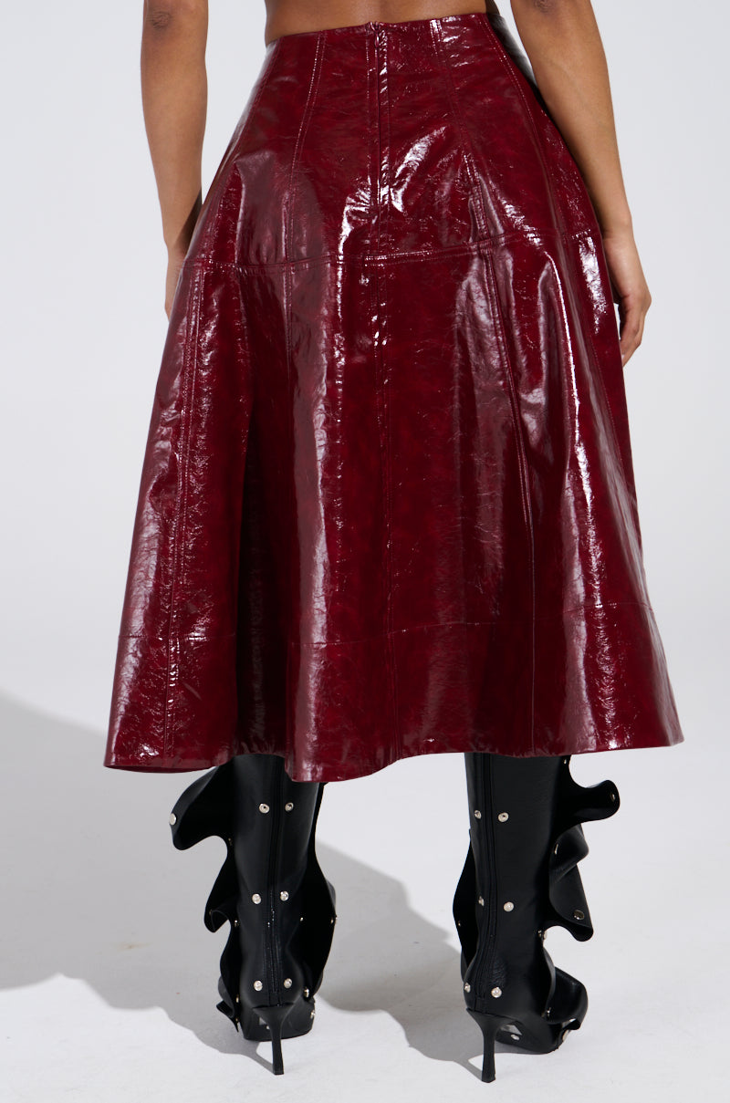 A person is wearing the burgundy THINK ABOUT IT FAUX LEATHER MIDI SKIRT with black high-heeled boots featuring wavy embellishments. The photo, taken from behind, showcases the standout outfit against a plain, light-colored background. 4