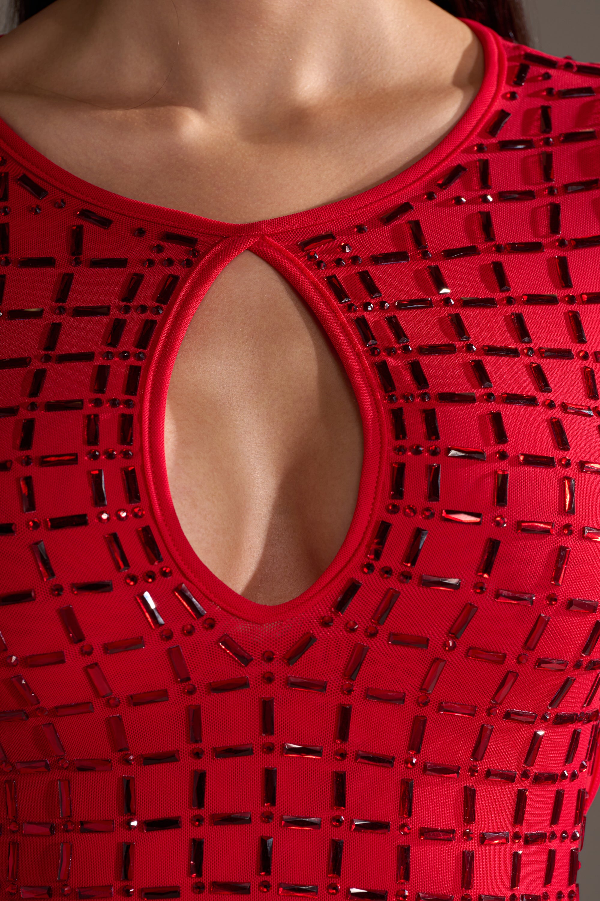 A close-up of a person wearing the ALL THAT SHINES RHINESTONE MINI DRESS, featuring a red bodycon fit with a keyhole chest cutout and shiny geometric rhinestone embellishments, focused on the upper chest and neckline.