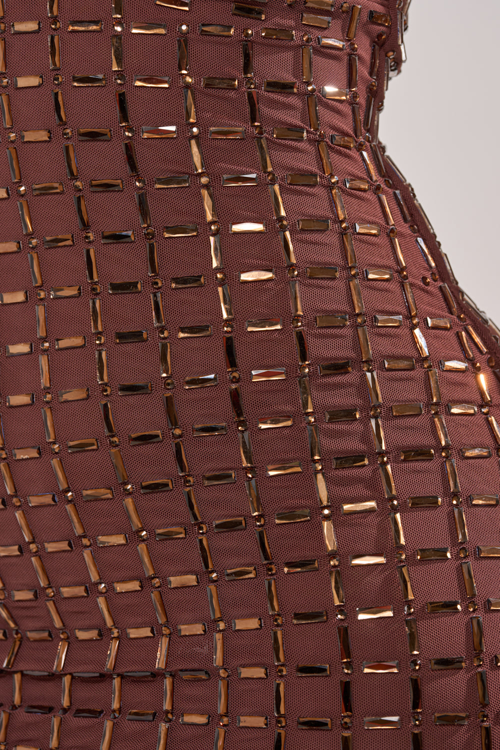 Close-up of the DANCE THE NIGHT AWAY RHINESTONE MINI DRESS, featuring brown mesh with a grid pattern and sparkling gold rectangular rhinestones that highlight its texture and shine on a curved surface. 7