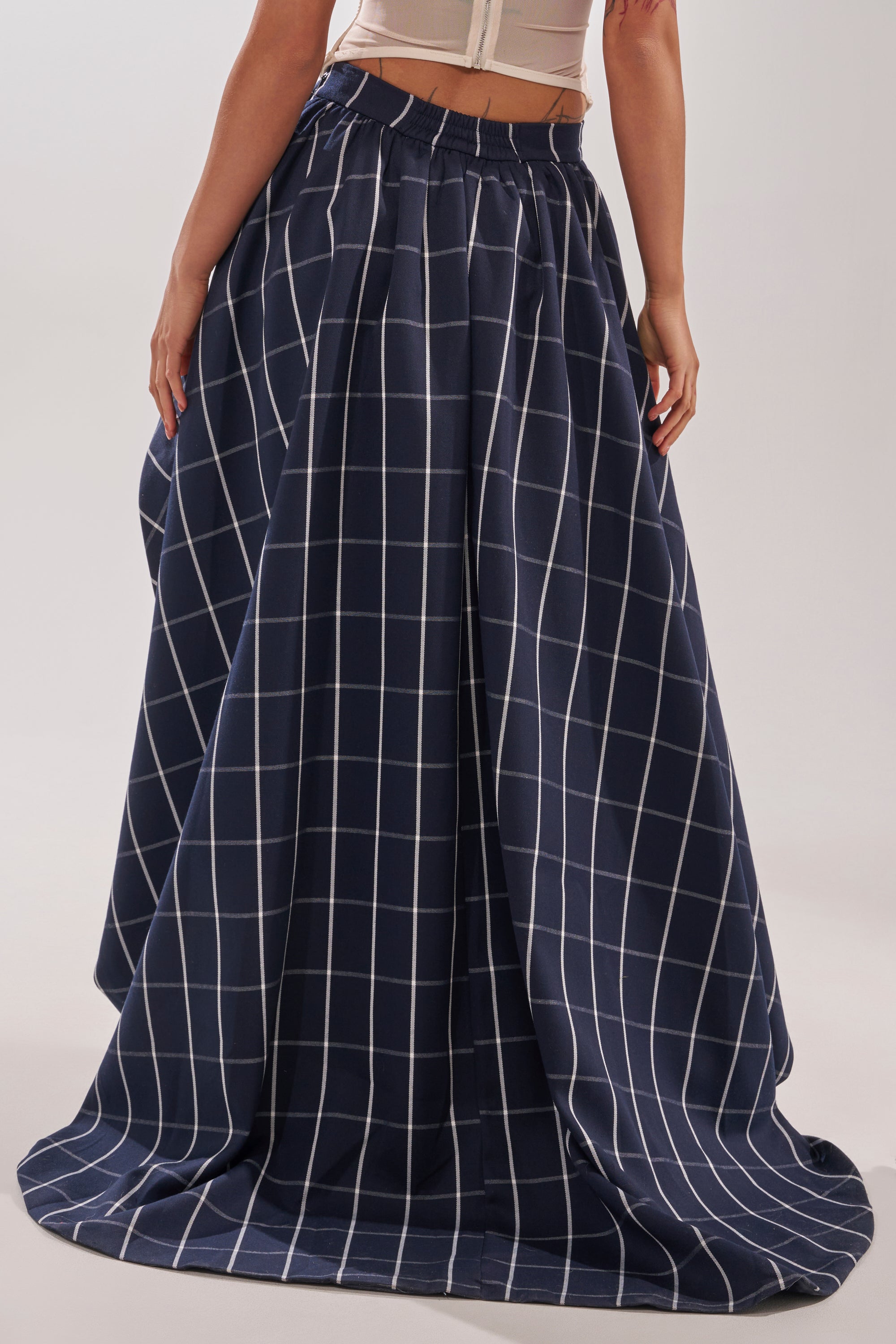 Wearing the MAKE A STATEMENT HIGH LOW SKIRT—a navy blue, asymmetrical plaid skirt with a white windowpane pattern—paired with a light fitted top for a modern, standout look. 4
