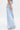 The lower half of a person stands sideways against a plain white background, wearing the IN CHARGE WIDE LEG DENIM PANT with a high-rise waist and raw hems for a vintage-inspired look.