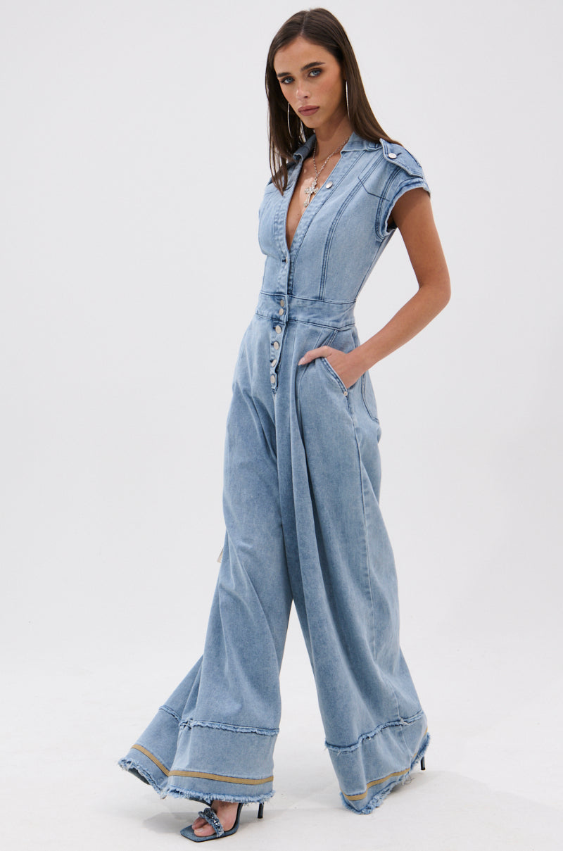 A woman with straight brown hair poses confidently in the AT LEAST I LOOK CUTE DENIM JUMPSUIT, a light-wash short sleeve piece featuring button details and pockets, standing against a plain white background for a utility-chic look.